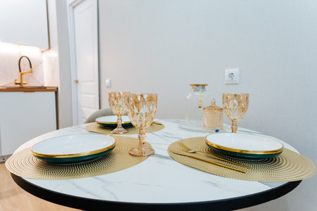 In a welldecorated kitchen, there is a round table adorned with elegant plates and beautiful wine glasses placed carefully on it, showing both functionality and style in the culinary spaceの写真素材