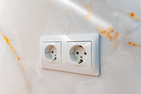 A detailed closeup view of a white electrical outlet that is installed on an elegant marble wall, showing the intricate textures and patterns of the marble, which contrast with the outletの写真素材