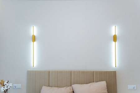 There are two unique and distinct light fixtures mounted on the wall just above the bed, beautifully illuminating the entire space with a warm and inviting glow that adds a cozy atmosphereの写真素材