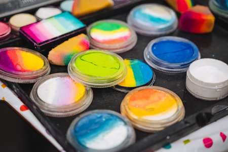 A tray that is entirely filled with a vivid assortment of colorful face paints, displaying a wide array of hues and shades meant for artistic expression, design, and decoration on skin surfacesの写真素材