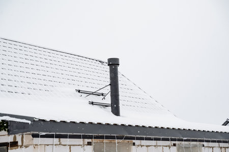 A house featuring a roof that has a chimney rising above it, beautifully adorned with a layer of fresh white snow that has accumulated on its surface, creating a picturesque winter sceneの写真素材