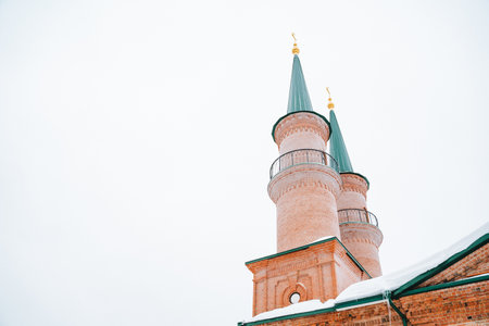 A magnificent brick building, featuring two striking minaret towers that rise elegantly from its roof and are beautifully blanketed in a layer of pristine snow, creating a captivating winter sceneの写真素材