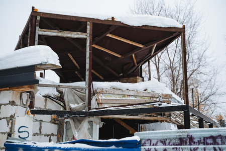 A structure that is currently undergoing the process of demolition is now entirely blanketed in a thick layer of snow, creating a stark contrast against the cold winter environmentの写真素材