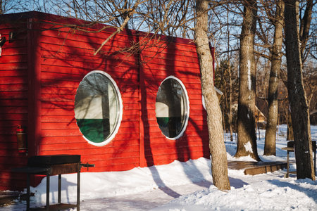A vibrant red cabin is beautifully nestled among snowcovered winter trees, featuring charming...