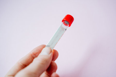 A person is strongly and firmly gripping a test tube that is topped with a bright red cap, which...