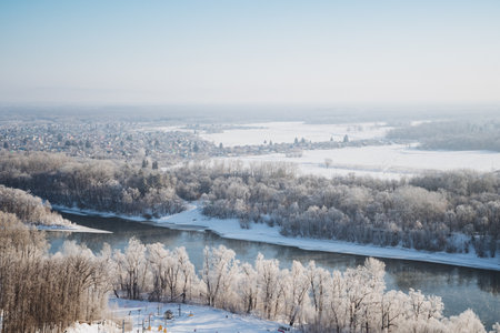 An aerial view showcases a tranquil river that gracefully winds through a landscape adorned by snowcovered trees, creating a stunning winter scene that captures the essence of natures beautyの写真素材