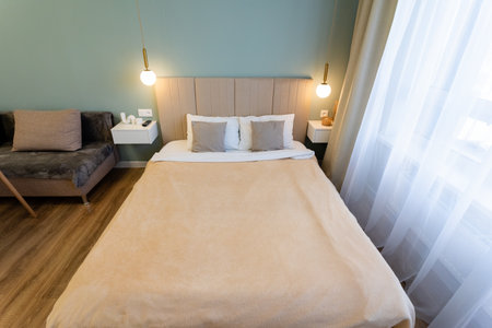 Imagine a cozy hotel room with a comfy bed, an inviting couch, and a large window bringing in natural light, creating a warm atmosphere for guests to unwind after a long dayの写真素材
