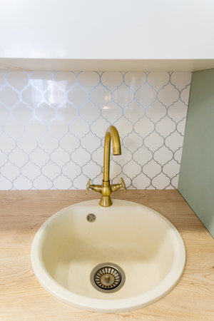In the heart of a beautifully designed kitchen, there is a sink featuring an elegant gold faucet that complements a stunning wooden countertop, creating a harmonious aestheticの写真素材