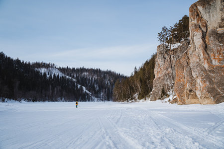 A solitary person is making their way along a snowy road that winds through the beautiful and serene mountains, surrounded by the tranquil winter wonderland of natures stunning landscapeの写真素材