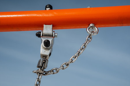 The image features a closeup of a metal hook and sturdy chain on a bright orange frame against a...