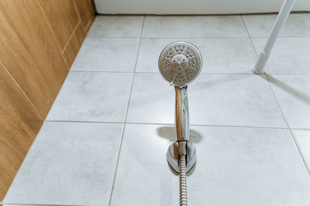 In a bathroom, there is a shower head that is currently positioned on a tiled floor. The tiles provide a stylish and functional base for the shower area, enhancing the overall aesthetic appealの写真素材