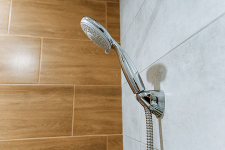 In a modern bathroom, a stylish shower head hangs from a tiled wall, merging aesthetics with...