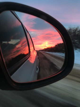 A beautiful sunset casts its vibrant colors, brilliantly reflected in the rear view mirror of a car...