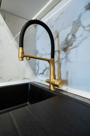 This is an impressive closeup image showcasing a luxurious gold faucet mounted on a sleek black sink located in a stylish kitchen, highlighting the elegance of household hardware made from brassの写真素材