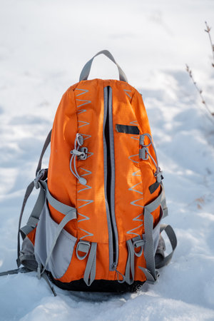 An eyecatching orange backpack is sitting all alone among the pristine white snow, its vibrant and...