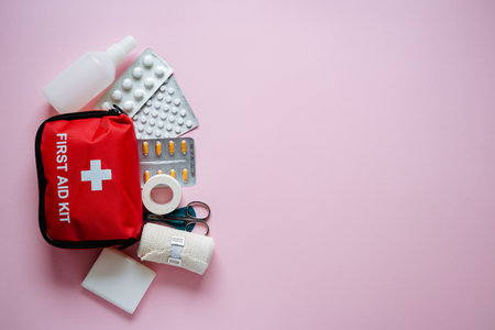 Discover essential first aid supplies including a red emergency kit, medications, bandages, and more, all showcased on a soft pink background for effective emergency careの写真素材