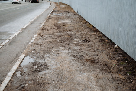 A muddy sidewalk lines a busy road with cars and various vehicles passing in both directions, creating a lively atmosphere filled with constant movement and transportation activitiesの写真素材