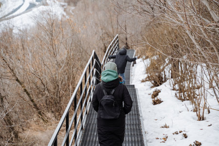 A couple is carefully walking down a snowy staircase, cautiously navigating the slippery steps. This...