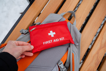 An individual is currently holding a first aid kit positioned above a backpack placed on the ground, which is essential for effectively managing emergencies or unexpected situations that may ariseの写真素材