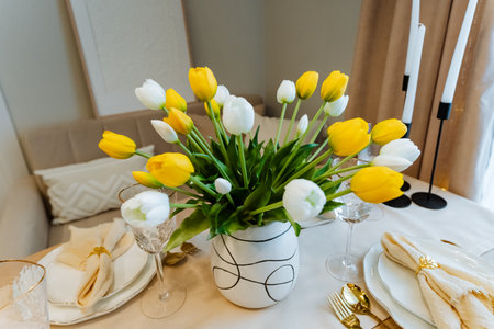 A beautiful table arrangement featuring vibrant yellow and white tulips in a stylish vase, ideal for spring events, dining, and decor inspirationの写真素材