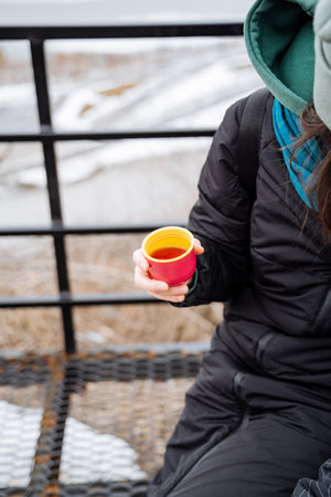 A woman sits back comfortably on her balcony, holding a steaming cup of tea in her hands, savoring...