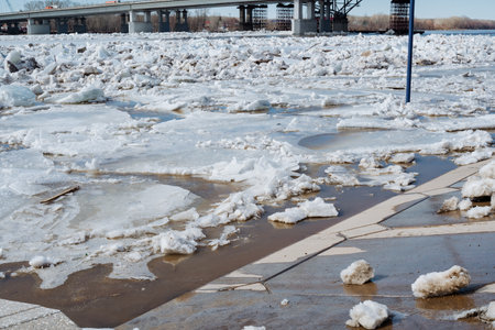 A sidewalk that is currently covered in a thick layer of ice and fresh fallen snow, with a bridge...