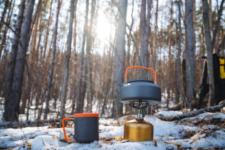 In a serene and picturesque winter landscape, a cozy cup along with a shiny kettle sit gracefully nestled in fluffy snow, surrounded by tall trees that stand majestically in the enchanting woodsの写真素材