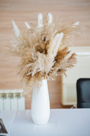 A beautiful white vase filled with vibrant and dried flowers enhances the tables appeal, adding natural beauty and charm that creates a warm, inviting atmosphere for all who see itの写真素材