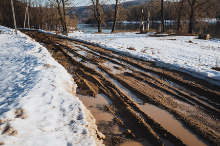 A muddy road that has snow piled up on the side of it, indicating the harsh and cold conditions of winter in this particular geographical area, showcasing the frozen environment and icy texturesの写真素材