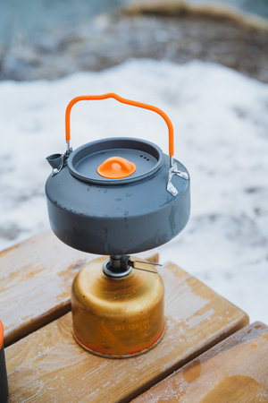 A kettle is positioned atop a gas cylinder, resting securely on a wooden table, creating a...