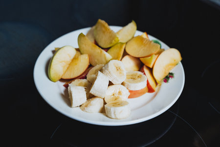 A pristine white plate, beautifully arranged, topped with an assortment of fresh sliced bananas and crispy apples for a delightful presentation that highlights the natural colors and texturesの写真素材