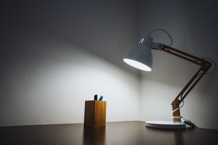 On a desk, there is a lamp that is positioned right next to a pen holder, creating a harmonious and functional workspace. The combination of these items enhances the overall aesthetic of the areaの写真素材
