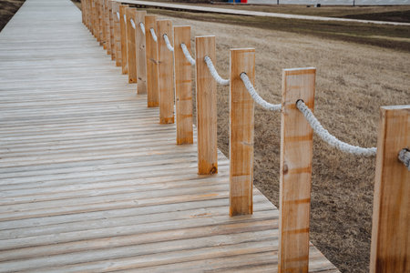 There exists a beautifully constructed wooden walkway that features a sturdy rope fence carefully placed along the side to enhance safety and aesthetic appeal while enjoying the surrounding natureの写真素材