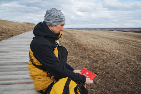 A man dressed in a bright yellow and black jacket is seated comfortably on a rustic wooden walkway,...