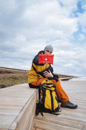 A hiker proudly showcases a vibrant red first aid kit on a rustic wooden path, clad in highquality...