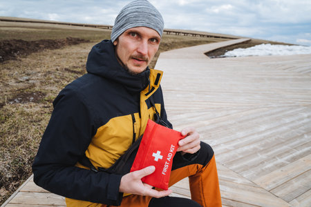 A man on a wooden walkway holds a first aid kit, highlighting the importance of being prepared in outdoor adventures to ensure safety and address emergencies effectivelyの写真素材