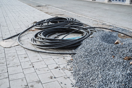 On the sidewalk, there is a pile of gravel accompanied by a bunch of wires scattered around, creating a scene common to construction sites and ongoing building projects in the areaの写真素材