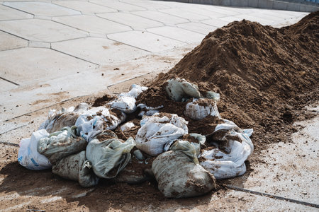Beside a large pile of dirt laid on the ground, there is also a considerable amount of bags filled with dirt sitting right there. Both are indicative of landscaping or construction activities nearbyの写真素材