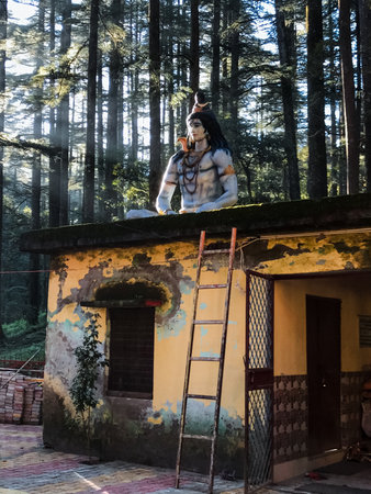 A breathtaking view of a magnificent Shiva statue atop a quaint structure surrounded by lush...
