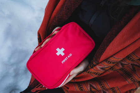 A person is confidently and securely holding a bright red first aid kit tightly in their hands, fully prepared for any potential medical emergencies that may possibly arise at any momentの写真素材
