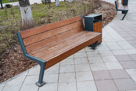 In a landscaped park, theres a charming wooden bench with an attached trash can, offering visitors a...