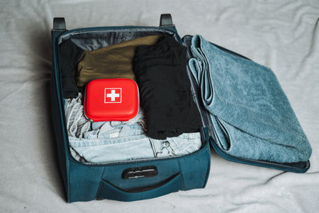 There is a blue suitcase that has been thoroughly packed with a variety of different clothes, along with a distinct red box that features a prominent symbol displayed clearly on its surfaceの写真素材
