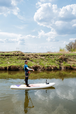 A skilled paddleboarder glides across a calm river, embodying joy from water sports. Surrounded by...