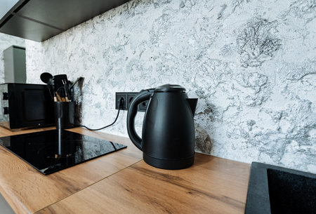 In a cozy kitchen, a sleek black kettle sits on a rustic wooden counter, adding charm and functionality, ready for use. This stylish and practical appliance is perfect for boiling waterの写真素材