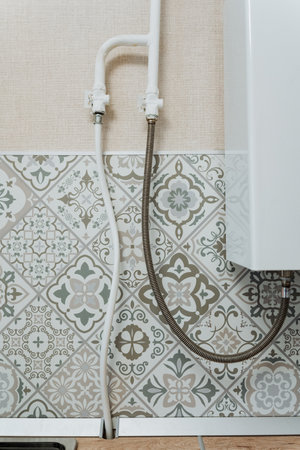 A flexible hose is firmly and securely fastened to a wall adjacent to a boiler unit, signifying a plumbing configuration that is likely essential for various functions in the bathroom or kitchenの写真素材