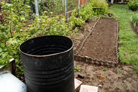 A large black barrel stands prominently in the center of a garden, surrounded by plants and colorful...