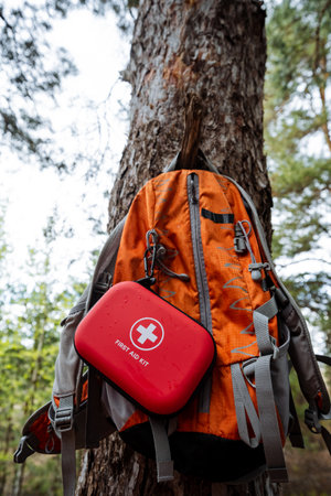 Explore the great outdoors safely This orange hiking backpack with a red first aid kit highlights essential gear, set against a serene forest backdrop for a truly enjoyable adventureの写真素材