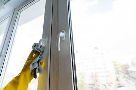 A person wearing bright yellow rubber gloves is meticulously cleaning a window with a soft cloth in order to make the glass pristine, spotless, and completely free of any smudges or streaksの写真素材