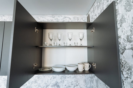 In a wellorganized kitchen, a cabinet stands tall with its doors wide open, revealing a neatly arranged shelf filled with an assortment of bowls and glasses, showcasing both functionality and styleの写真素材