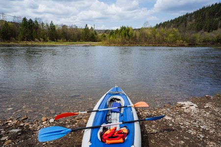 A colorful kayak rests on a sunlit shore, surrounded by tranquil waters and lush trees, creating a...